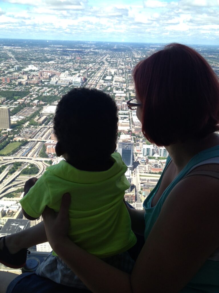 Diana holding one of her children at a window high above the city