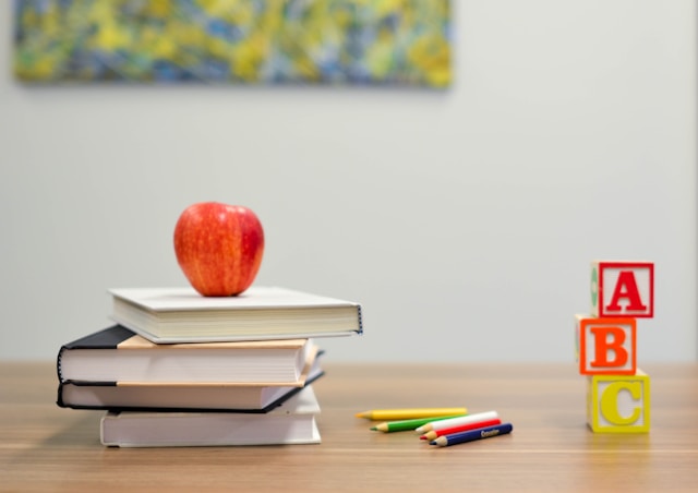 An apple sitting atop a pile of schoolbooks