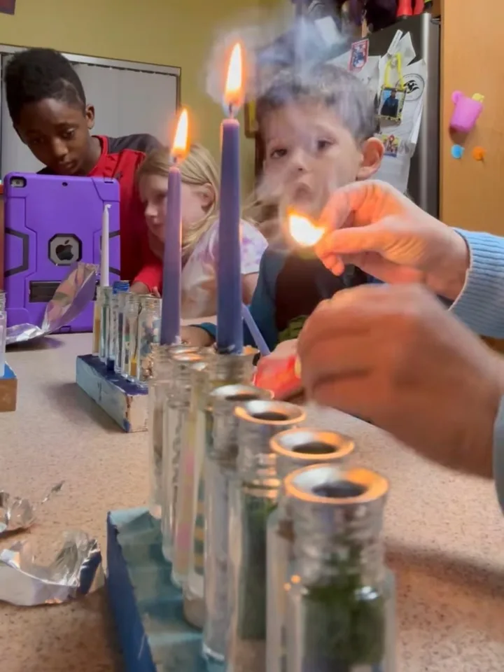 Children watching as candles are lit on a homemade Hanukkah menorah