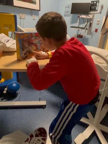 A boy playing with a new toy at the bedside table in his hospital room